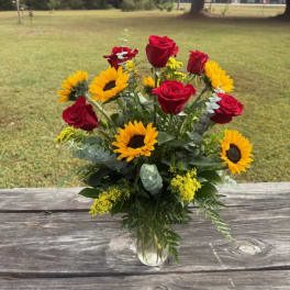 Bouquet of red roses and yellow sunflowers in a clear glass vase