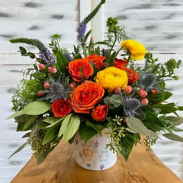 Colorful bouquet of orange and yellow roses in a patterned container