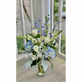 Tall bouquet of white roses and blue flowers in a clear glass vase