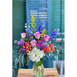 Colorful mixed bouquet in a clear glass vase with pink roses and blue flowers