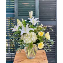 White lilies and pale yellow blooms arranged in a clear glass vase
