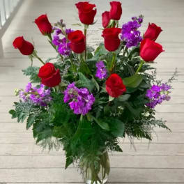 Tall bouquet of red roses and purple flowers in a clear glass vase