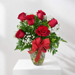 Red roses and white baby's breath in a glass vase with a red bow