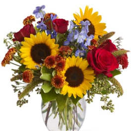 Bouquet of sunflowers, red roses, and blue flowers in a clear glass vase