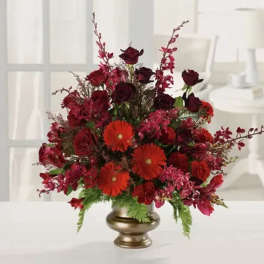 Red floral arrangement in a gold vase with orange daisies