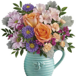 Bouquet of orange roses, pink alstroemeria, and purple daisies in a turquoise mug vase