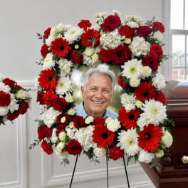 Red and white floral funeral wreath on an easel with a photo in the center
