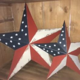 Two patriotic star decorations in red, white, and blue against a wooden wall