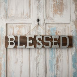 Wooden sign reading "BLESSED" hanging on a distressed white door