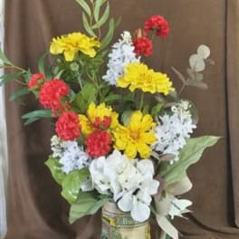 Colorful flower arrangement in a decorative can with red, yellow, white, and blue blooms