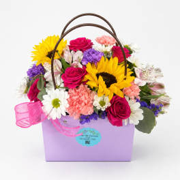 Mixed flower basket with sunflowers, roses, and carnations in a lavender container