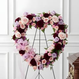 Heart-shaped floral wreath on a stand with pink, lavender, and burgundy flowers