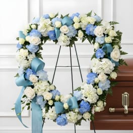 Heart-shaped floral wreath with white and blue flowers on a stand