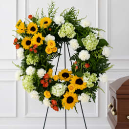 Large floral wreath on a stand with sunflowers, white blooms, and orange roses