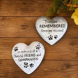 Two heart-shaped memorial stones with paw prints and text on a wooden surface.