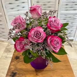 Pink roses arranged in a purple vase with small filler flowers