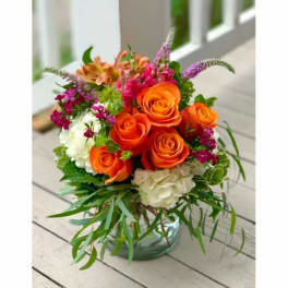 Bright mixed bouquet of orange roses, white hydrangea, and pink accents in a glass vase