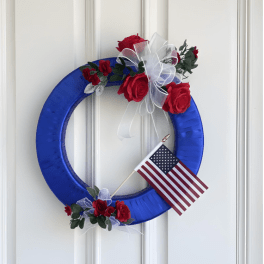 Blue wreath with red roses, white ribbon, and a small American flag