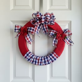 Red wreath with plaid bows and small red flower accents on a white door