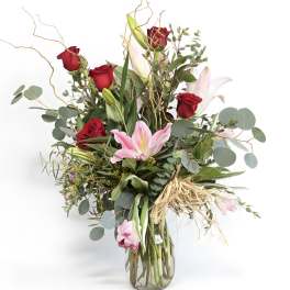 Red roses and pink lilies in a glass vase with greenery