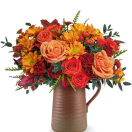 Orange and red flower arrangement in a brown pitcher vase