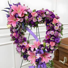 Heart-shaped floral wreath with pink lilies and purple flowers on a stand