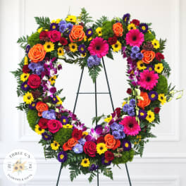 Heart-shaped floral wreath with roses, daisies, and orchids on an easel