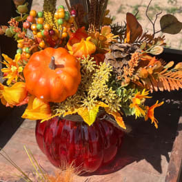 Autumn floral arrangement with a pumpkin and red glass vase