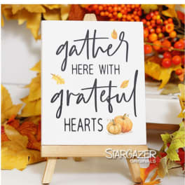 Fall sign on a small wooden easel reading "gather here with grateful hearts"