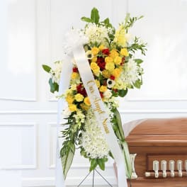 Tall funeral spray of yellow, red, and white flowers with a ribbon on an easel