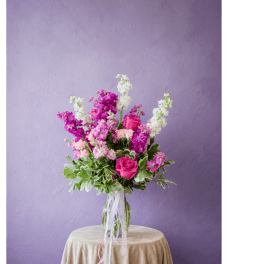 Pink and white flower arrangement in a clear glass vase on a draped table