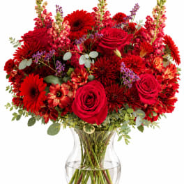 Red roses and mixed red flowers in a clear glass vase