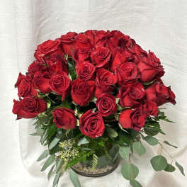 Red rose bouquet in a glass vase with trailing greenery