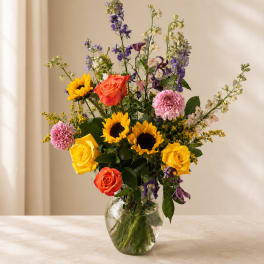 Mixed bouquet of roses, sunflowers, and purple blooms in a clear glass vase