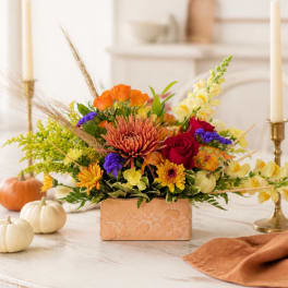 Autumn floral arrangement in a peach rectangular vase with pumpkins nearby