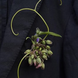 Small boutonniere with green buds and purple accents on a dark jacket