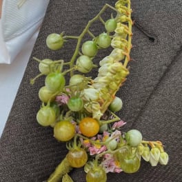 Boutonniere with green berries, pale blossoms, and pink flowers on dark fabric