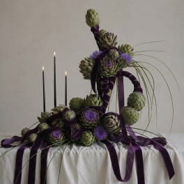 Artistic arrangement of artichokes with purple ribbon and candles