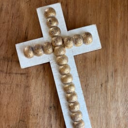 Decorative cross made of white wood and gold beads on a wooden surface