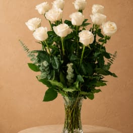 White roses arranged in a clear glass vase with greenery
