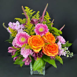 Orange roses and pink gerbera daisies in a clear square vase