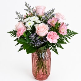 Pink roses, carnations, and white daisies in a pink glass vase