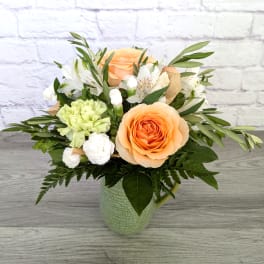 Peach roses and white flowers arranged in a green mug vase