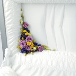 Purple and yellow floral spray arranged on a white casket