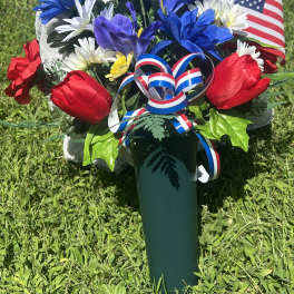 Red, white, and blue floral arrangement in a green vase with an American flag