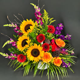 Colorful flower arrangement with sunflowers, roses, and red daisies in a white basket