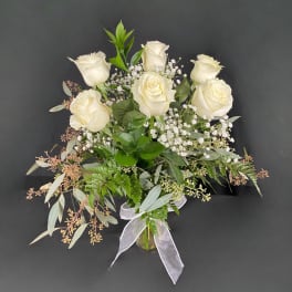 White roses arranged in a glass vase with baby's breath and greenery