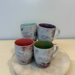 Four floral quote mugs with colored interiors arranged on a round tray