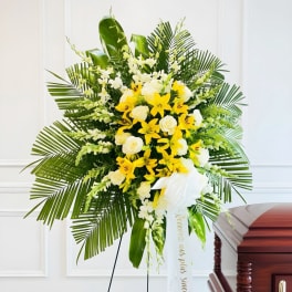 Yellow and white floral standing spray with palm fronds and a white ribbon
