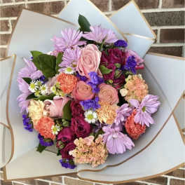 Mixed bouquet of pink, purple, and peach flowers wrapped in white paper